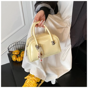 Detail view of cream yellow patent leather pillow bag with silver metal ring and pearl charm