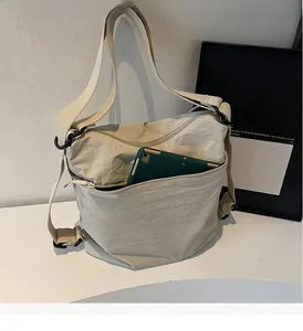 Detail showing high-capacity front pocket of beige nylon bag with a green tablet inside