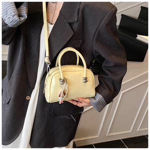 Detail of a shiny yellow Boston bag featuring a pearl charm and detachable shoulder strap
