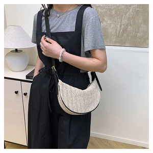 Detail of straw woven half-moon bag with black trim and adjustable shoulder strap