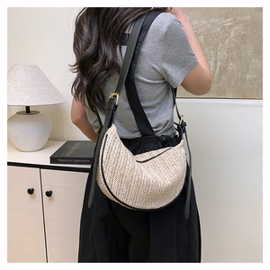 Detail view of woven straw crescent bag with black leather strap and golden metal buckle