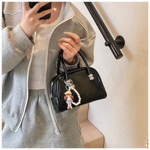 Detail of black patent leather pillow bag with pearl charm and doll keychain accessory