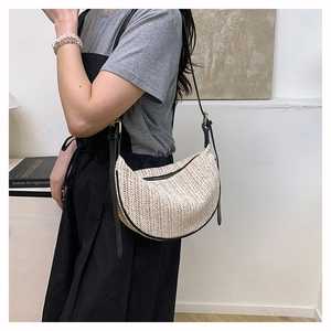 Detail of woven straw crescent bag with black leather trim and adjustable gold buckle