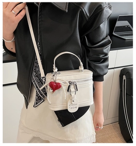 Detail of white box bag featuring a red heart charm and decorative pearl chain