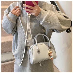 Detail of light grey Boston bag with elegant pearl pendant and cartoon doll charm on strap