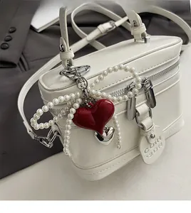 Detailed view of white leather handbag with red heart charm and decorative pearl strap