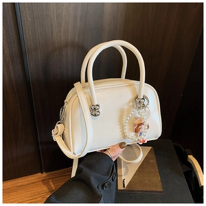 Close-up of white glossy pillow bag with pearl charm and adjustable shoulder strap