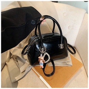 Close-up of black glossy pillow bag with silver zippers and pearl doll charm detail