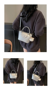 Détail d'un sac seau tressé argenté avec fermoir magnétique et pompon décoratif
