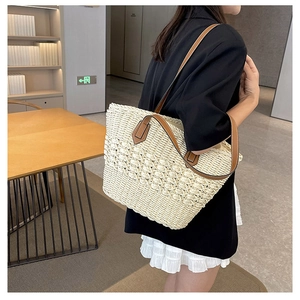 Detail of bohemian woven straw tote bag with brown leather handles and textured weave