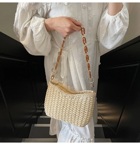Detail of hand-woven beige straw bag with brown acrylic chain link shoulder strap