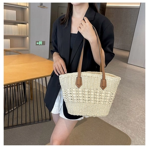 Detail of hand-woven straw tote bag with brown leather shoulder straps on a female model