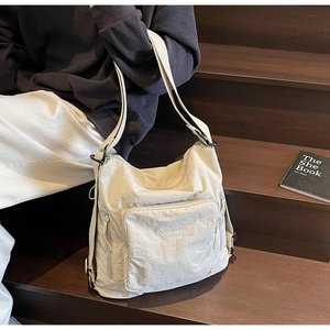 Detail of beige nylon tote bag with multiple zippers and embroidered text on stairs