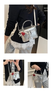 Detailed view of silver vanity bag with heart and pearl charms and branded logo tag