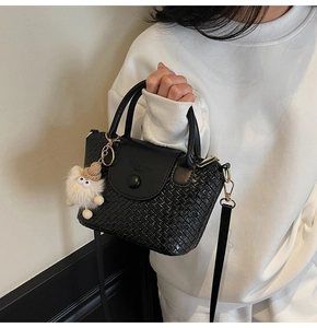 Détail d'un sac seau noir tressé avec un charmant pendentif en peluche blanche
