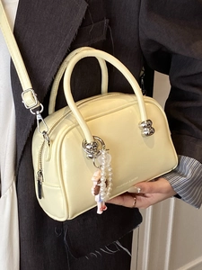 Chic cream Boston handbag with pearl charm shown on a stylish model in dark suit