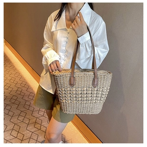 Detail of hand-woven straw tote bag with brown leather straps and hollow mesh pattern