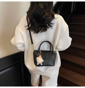 Détail du sac seau noir tressé avec bandoulière en cuir porté au dos par un modèle