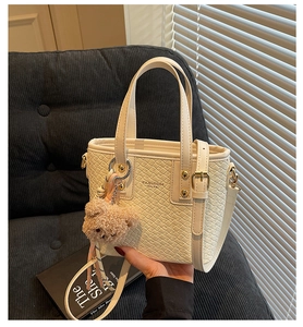 Detailed macro of cream bucket bag with woven texture and brown teddy bear charm