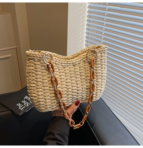 Detail of woven straw tote bag featuring amber acrylic and gold chain link strap