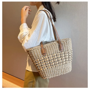 Close-up of a woven straw tote bag featuring intricate openwork patterns and brown leather straps