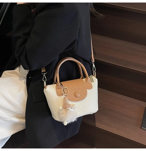 Détail du sac seau tissé avec bordure en cuir marron et breloque chapeau en peluche