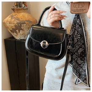 Dettaglio borsa a sella nera lucida con fibbia argento e foulard in seta motivo paisley