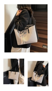 Detailed close-up of beige twill woven tote bag with slim black handles and metallic charms