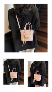 Detailed view of pink woven bucket bag with teddy bear charm and striped ribbon accent