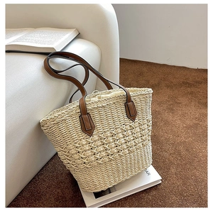 Close-up of woven straw handbag featuring hollow patterns and brown leather straps