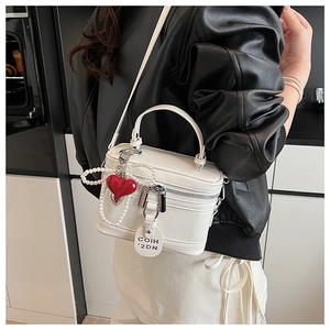 White patent leather box bag with pearl chain and red heart charm worn with black outfit