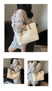 Close-up detail of large beige woven tote bag with brown leather handles and tassel charm