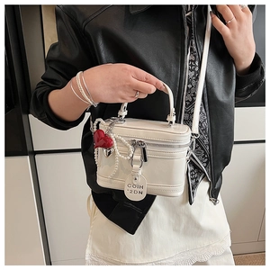 Detail of white patent leather box bag with red heart charm and pearl chain accessory