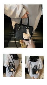 Detail of black woven texture bucket bag featuring a plush bear charm and striped ribbon