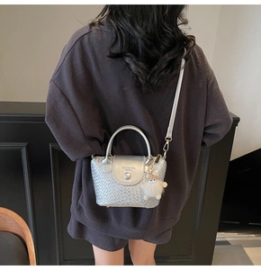 Détail de sac seau argenté à texture tressée avec un petit charme en peluche blanc