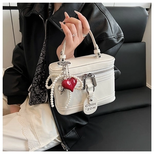 Macro view of white box-shaped handbag featuring heart charms and pearl chain details