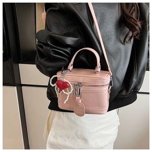 Pink box crossbody bag with heart charm and pearl strap detail shown on black leather jacket
