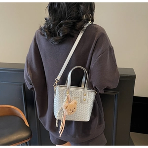 Close-up of silver woven texture bucket bag with a teddy bear charm and striped scarf