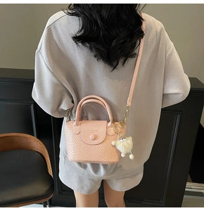 Détail du sac seau en cuir tressé rose avec pendentif en peluche sur un mannequin