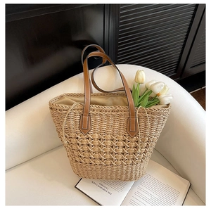 Close-up of the textured straw weave and brown leather handle on a stylish beach tote bag