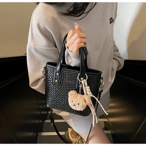 Detail of black woven texture tote bag with a cute beige plush bear charm on the handle