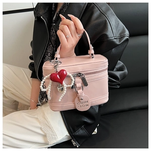 Pink glossy mini box bag with heart charms and pearl chain on a black leather seat