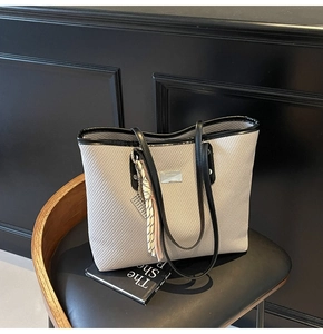 Detail of grey woven tote bag featuring black leather handles and silver metal logo plate