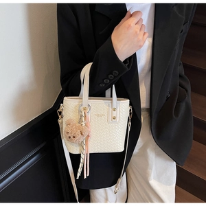 Detail of woven texture bucket bag with plush bear charm and silk scarf handle decor