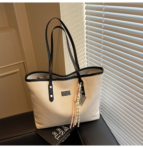 Detail of cream woven tote bag with black leather handles, tassel and JINGPIN logo