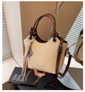 Gros plan d'un sac seau en daim beige avec anses en cuir marron et pendentifs déco