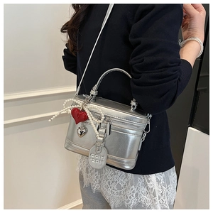 Detailed macro of silver metallic box bag featuring pearl bow and heart charm pendants