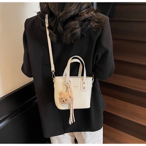 Close-up of white woven bucket bag with teddy bear charm and ribbon on dark stairs