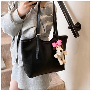 Detail of black faux leather tote bag with long straps and cute puppy charm on stairs