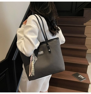 Detail view of large grey tote bag with woven texture and decorative tassel charm